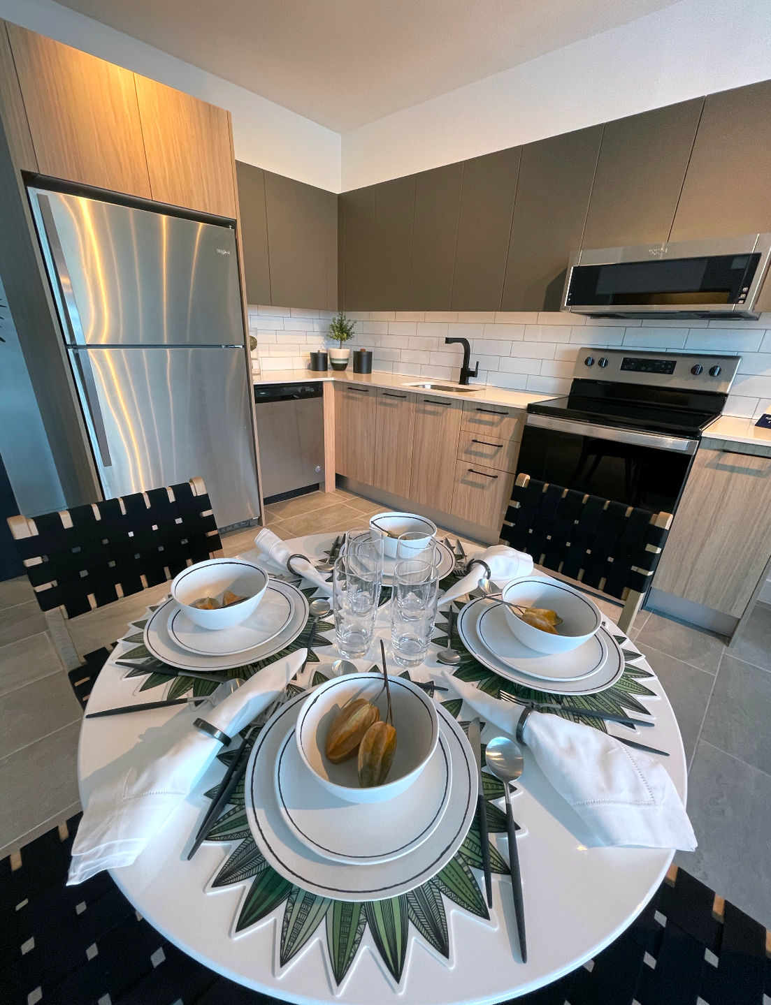 Modern apartment kitchen with stainless steel fridge, oven, microwave, and a round dining table set for four.
