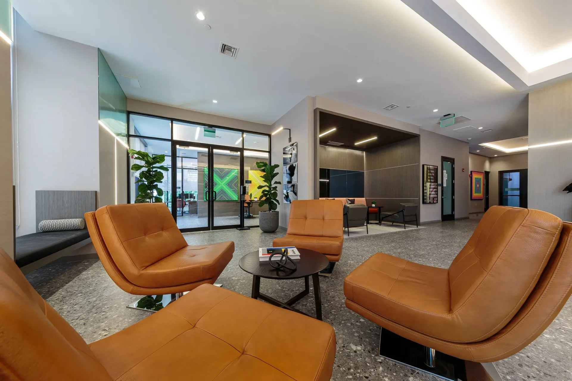 Modern apartment lobby with orange leather lounge chairs, glass entry doors, and greenery.