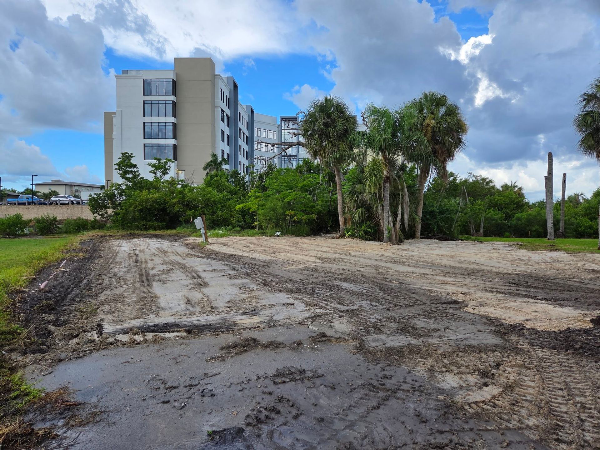 Empty dirt lot beside a modern apartment building under a cloudy blue sky
