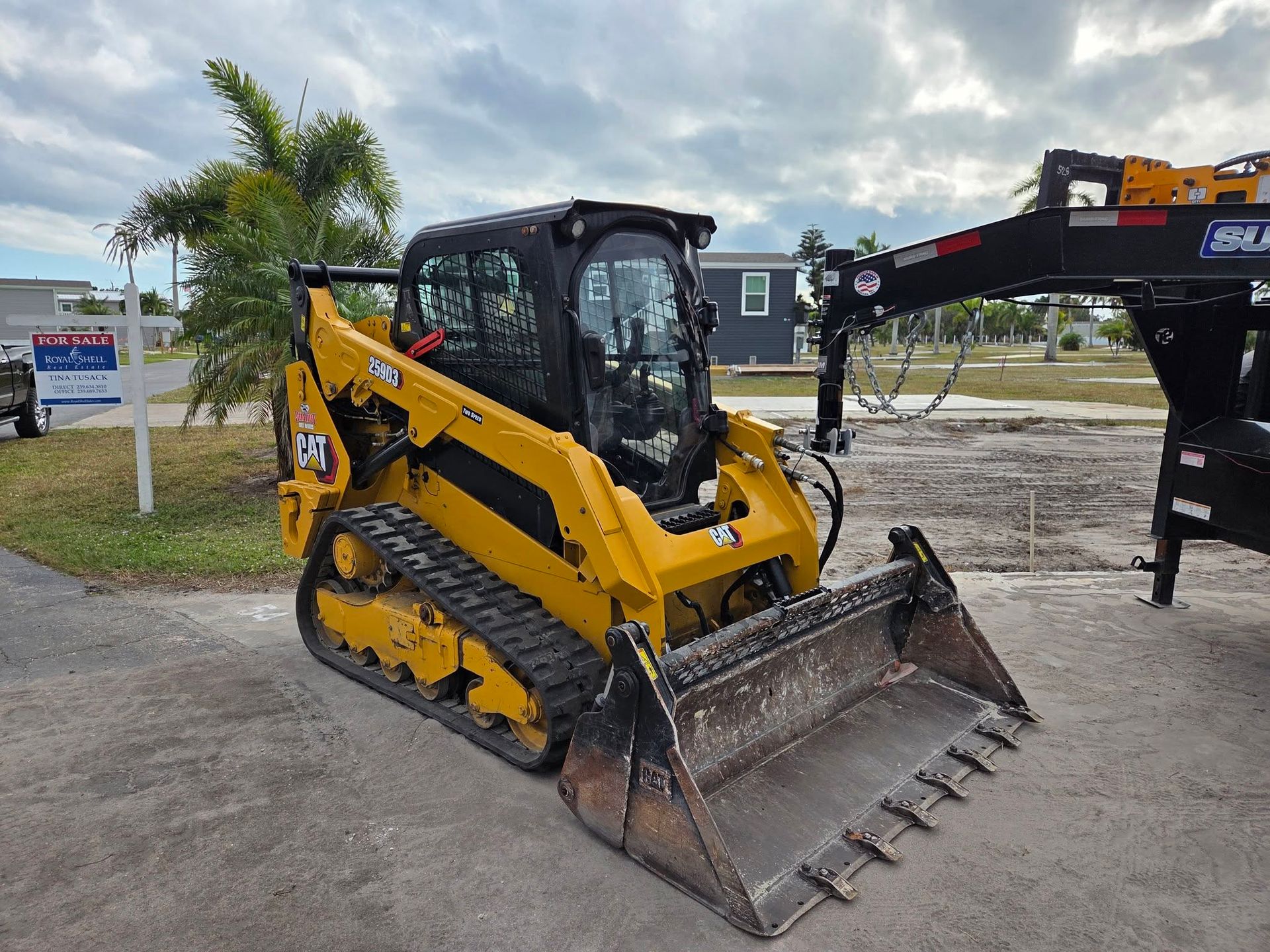 Yellow compact track loader with a bucket in an outdoor equipment lot under cloudy skies