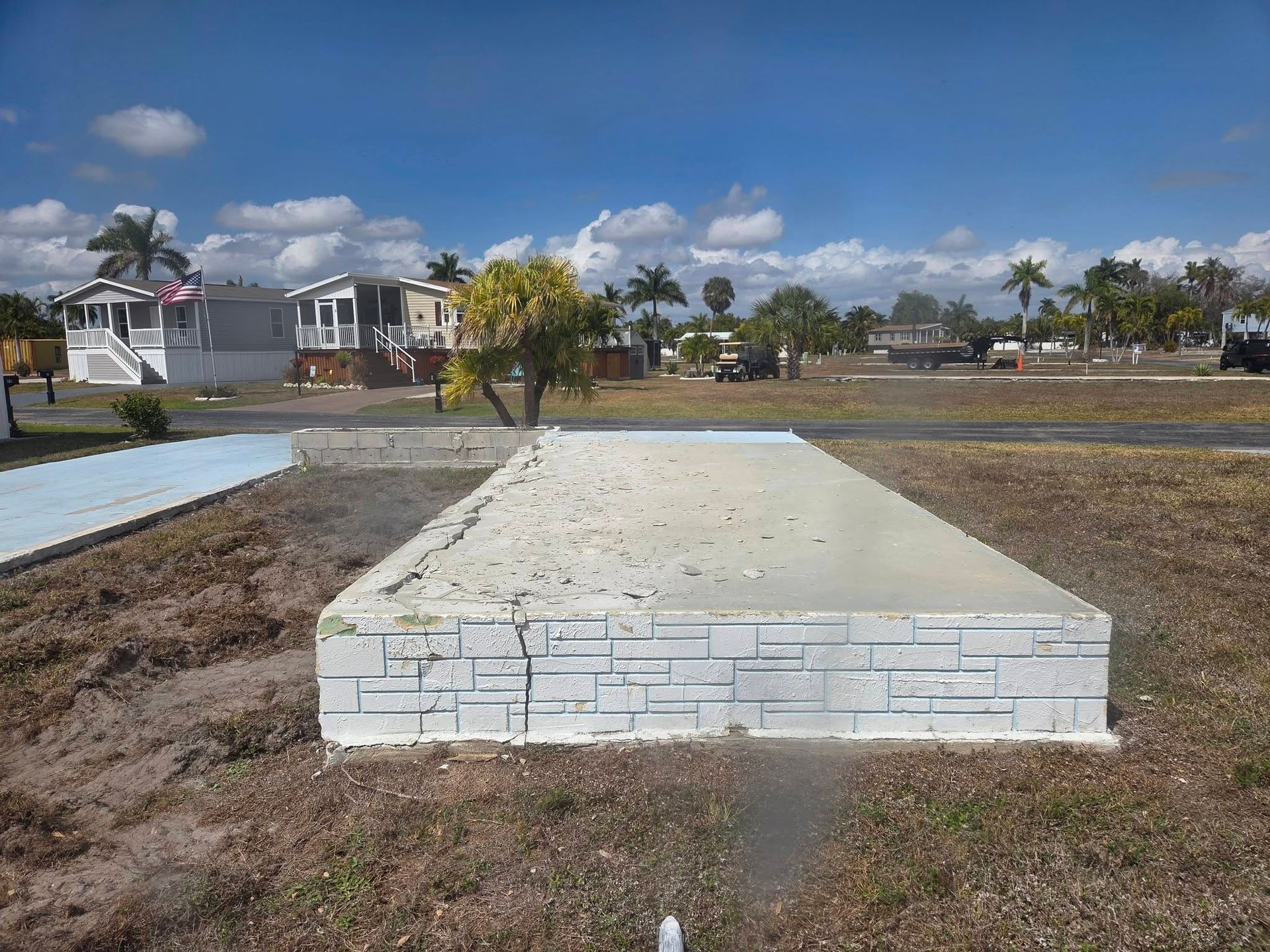 Raised concrete slab in an open lot, with a white brick front and houses under a cloudy sky in the background.
