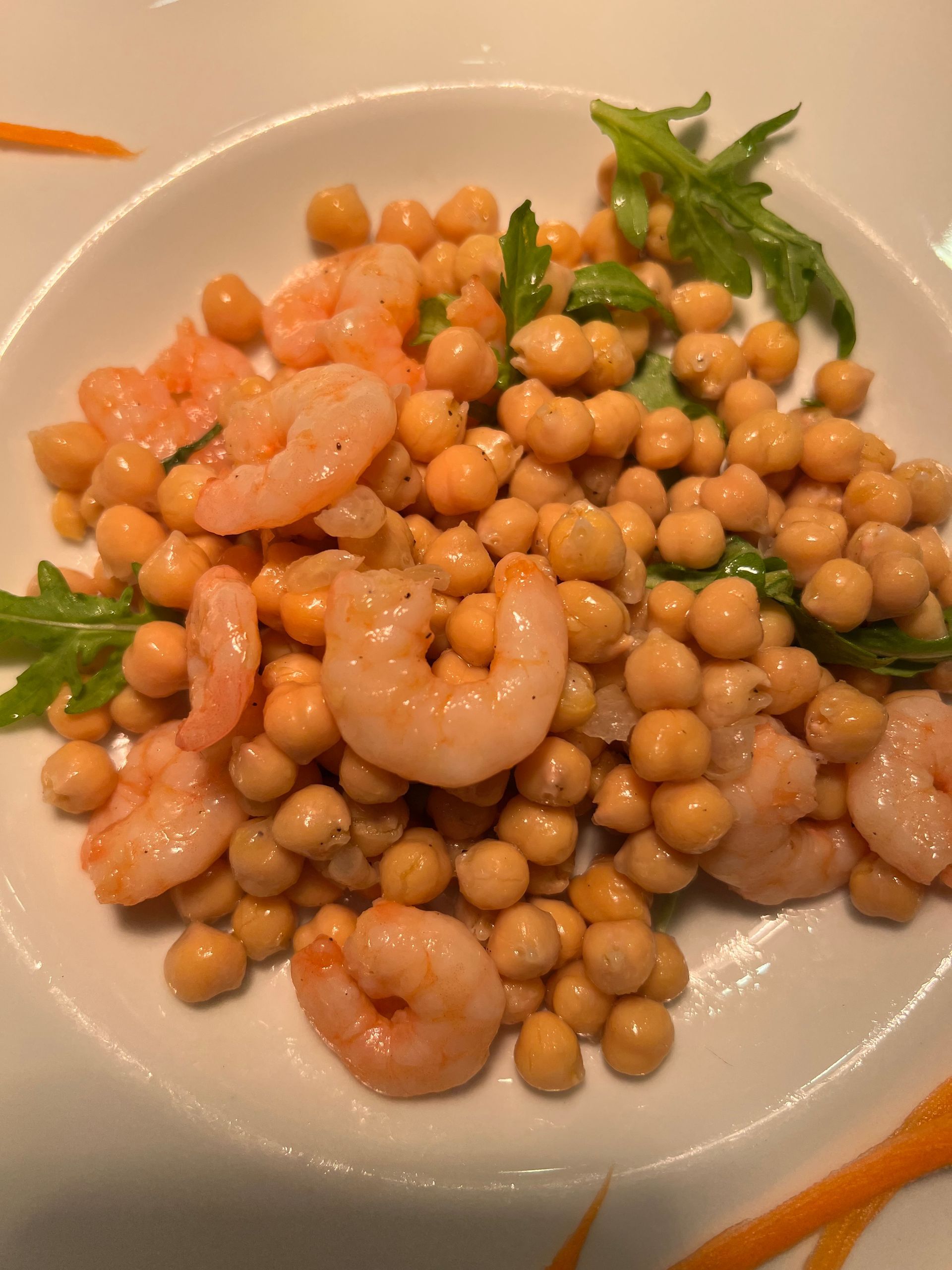 Insalata di ceci e gamberi su un piatto bianco, guarnita con rucola.