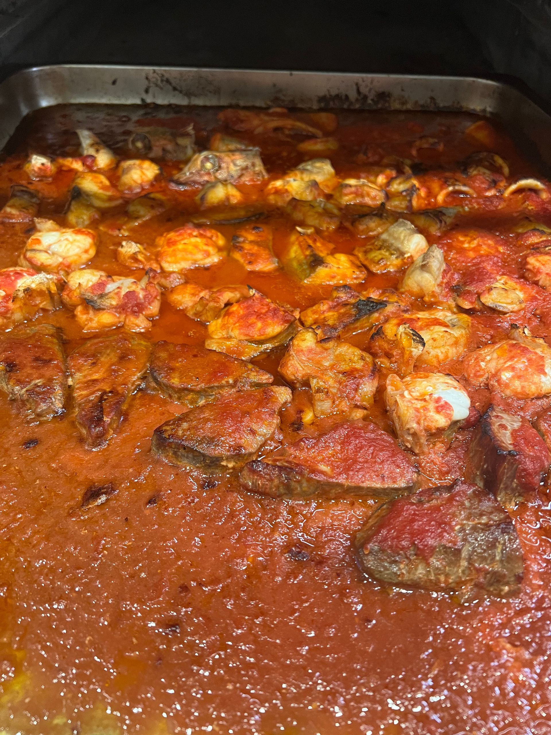 Pesce al forno in salsa rossa, in una teglia rettangolare di metallo.