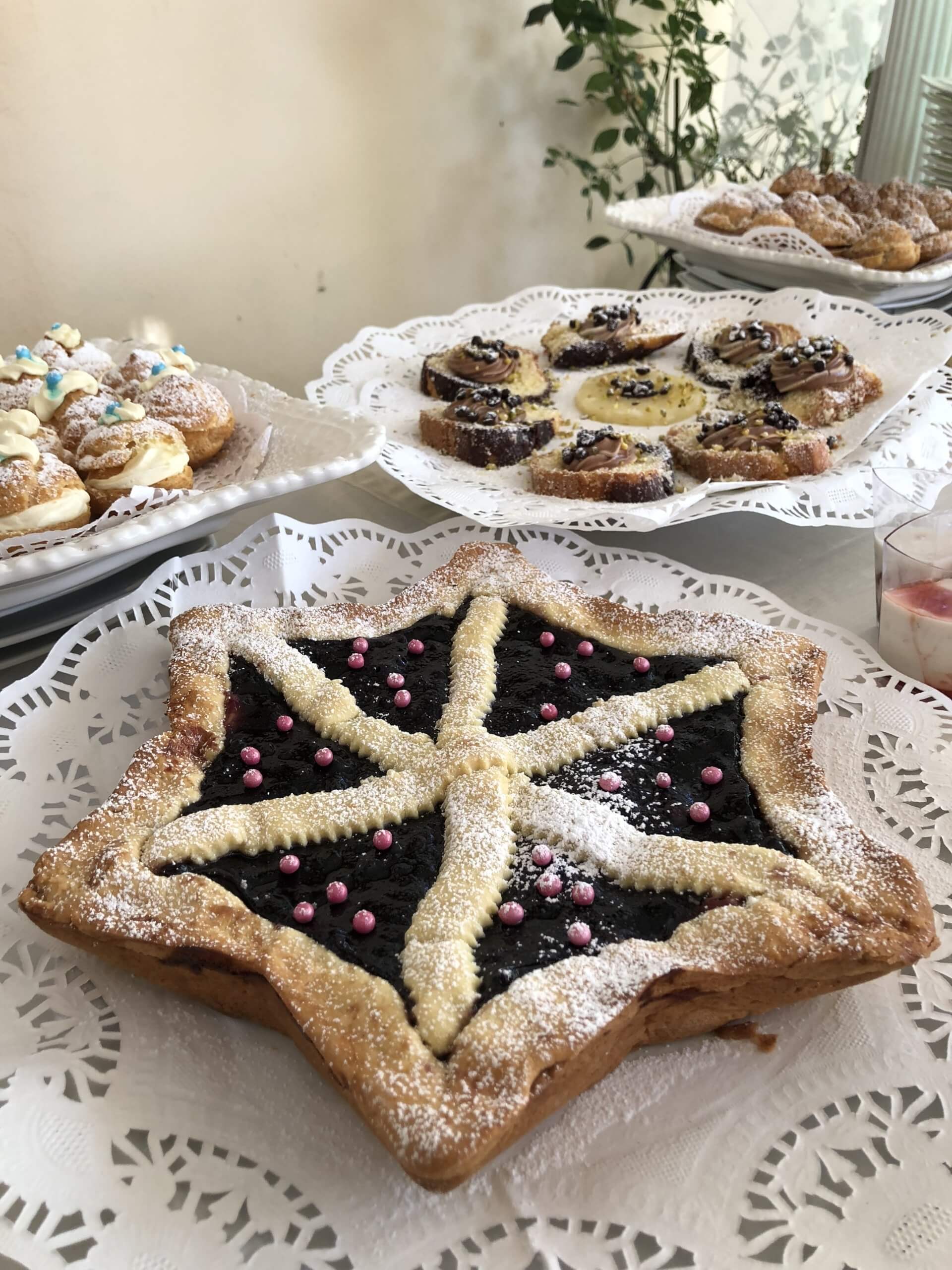 Pasta sfoglia a forma di stella con ripieno di frutti di bosco, circondata da altri dessert su un tavolo bianco.