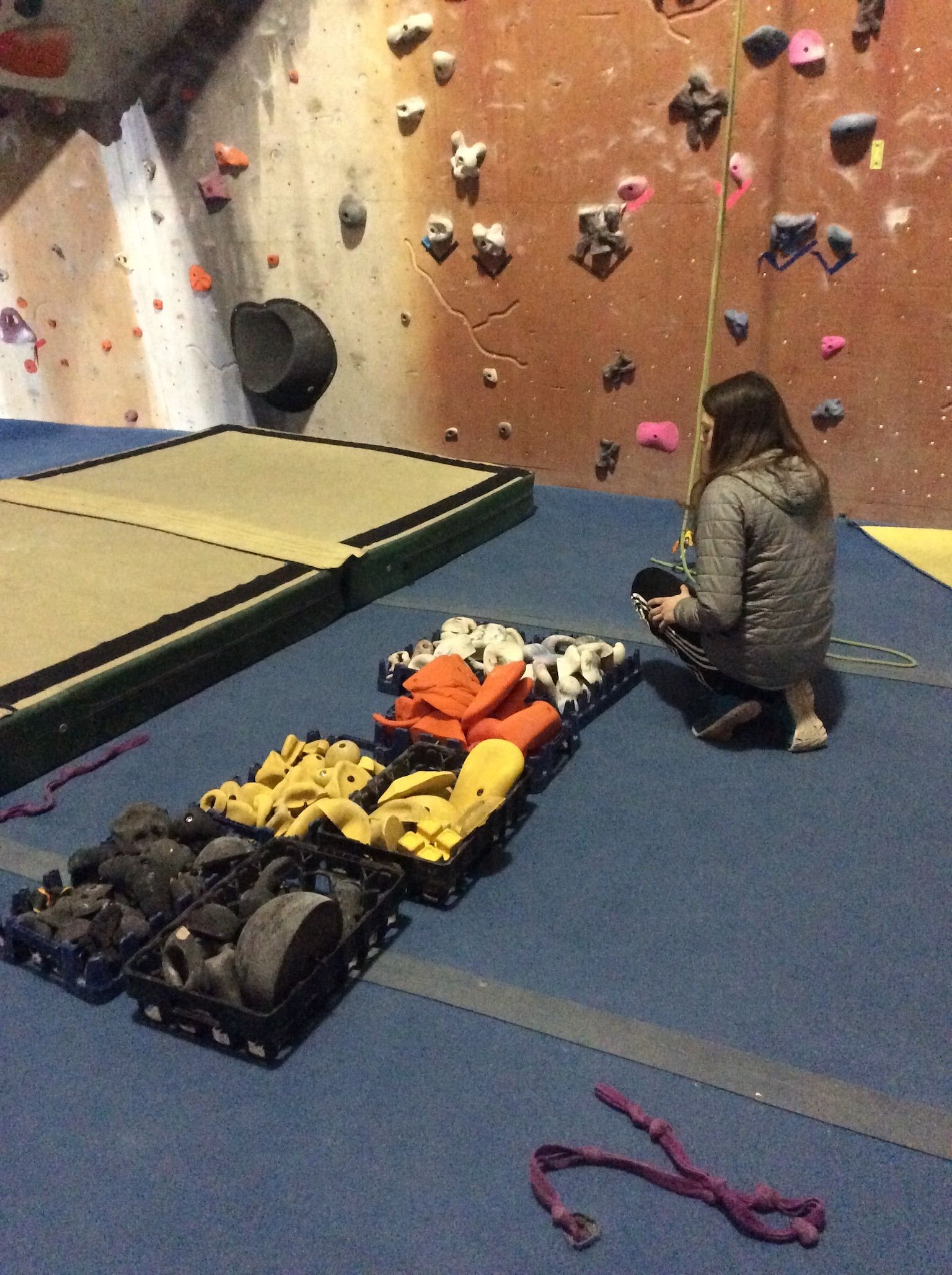 A woman sits on the floor in front of a climbing wall