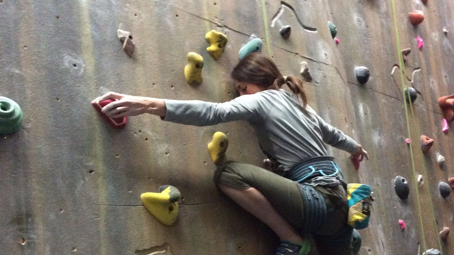 A woman is climbing up a climbing wall.