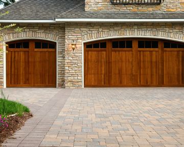 Stone house facade with two wooden garage doors and a paved driveway