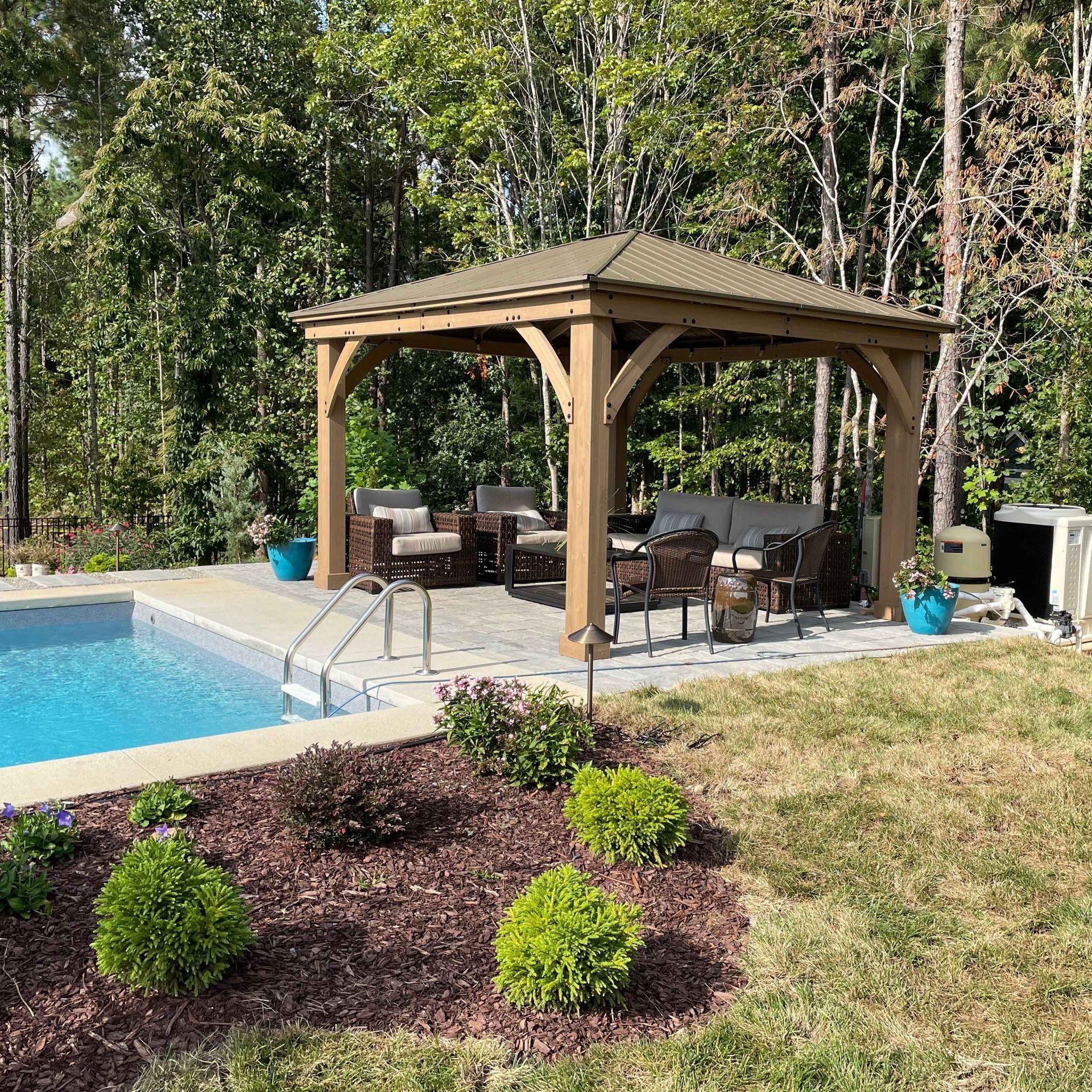 Backyard poolside gazebo with patio furniture beside a landscaped lawn and trees