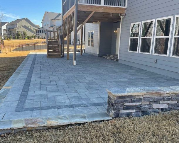 Stone patio beside a gray house with raised deck steps and a small retaining wall