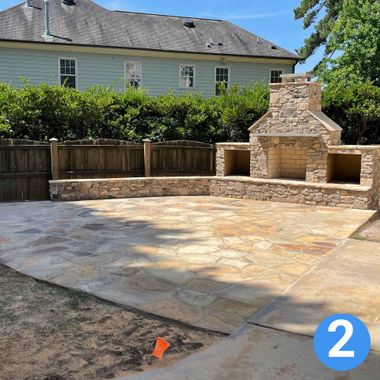 Stone patio with built-in outdoor fireplace and seating wall in a backyard