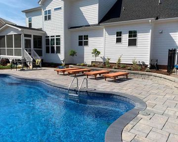 Backyard pool beside a white house with patio seating and lounge chairs on a stone deck