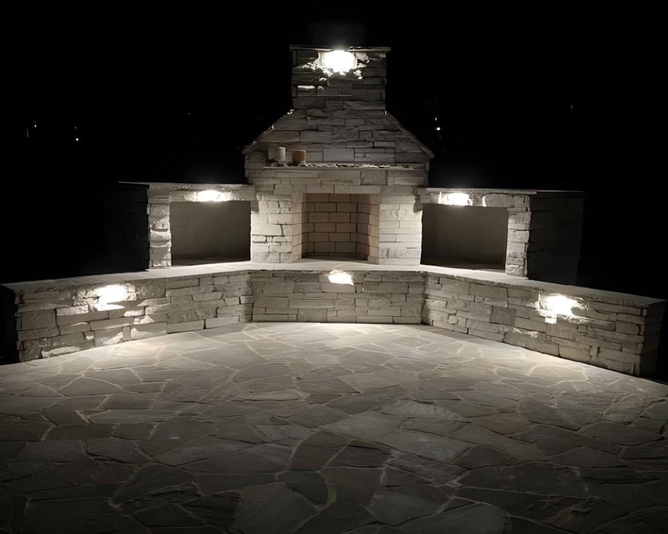 Illuminated stone outdoor fireplace and curved wall seating area at night