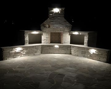 Illuminated stone outdoor fireplace and curved wall seating area at night