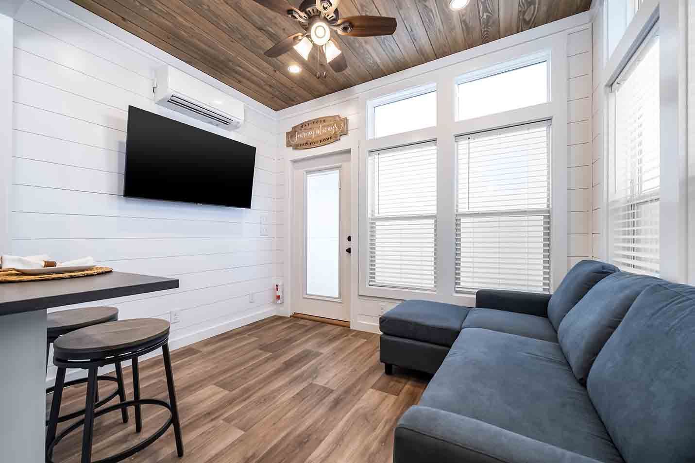 Cozy living room with blue sectional, wall-mounted TV, wood floors, and bright windows