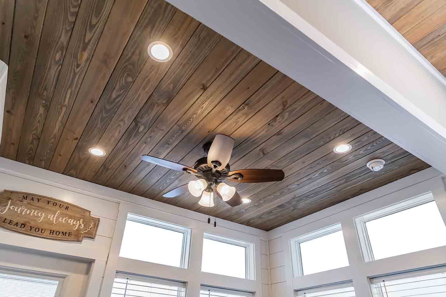 Wood-paneled vaulted ceiling with recessed lights, a ceiling fan, and tall windows in a bright room