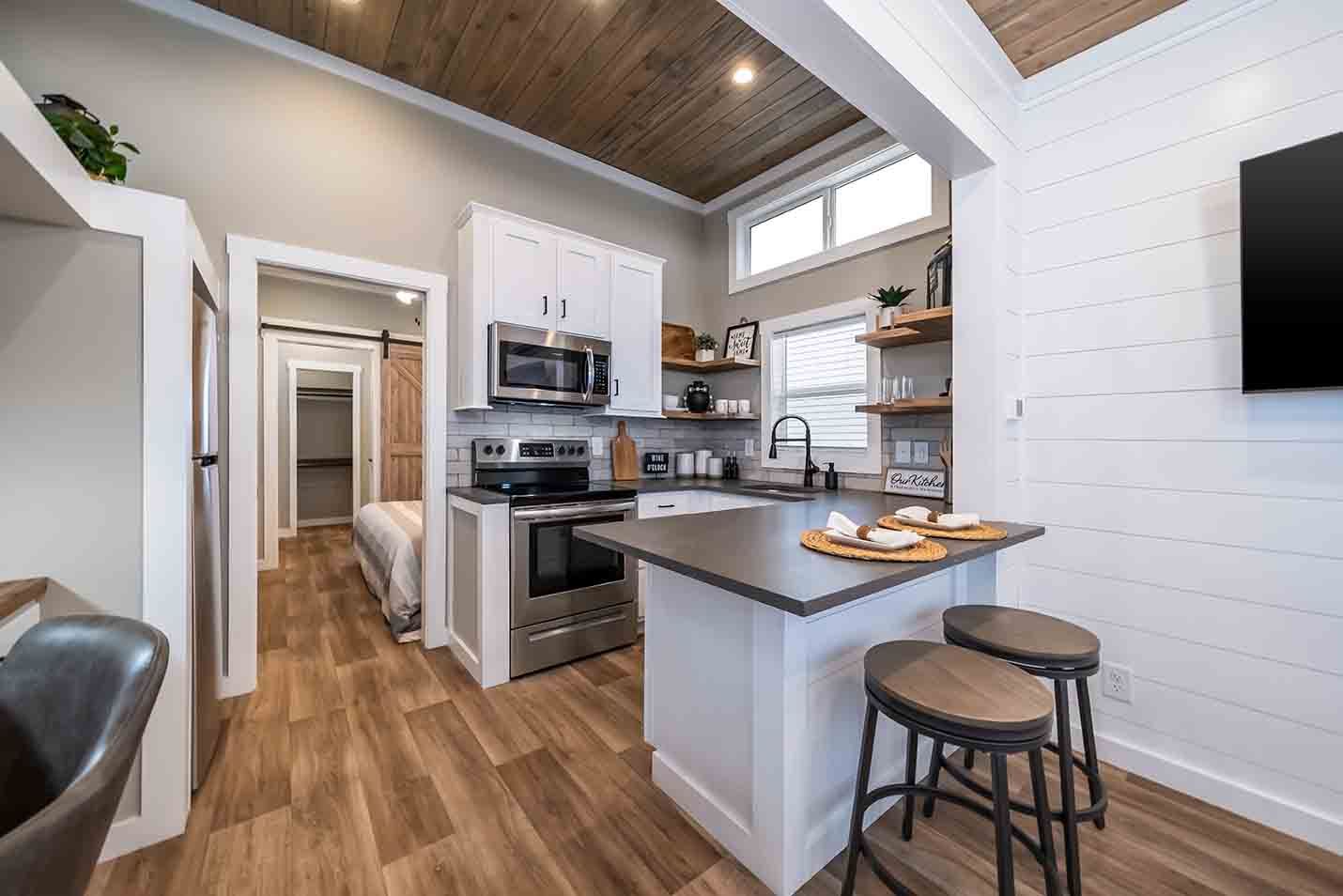 Modern kitchen with white cabinets, gray island, wood ceiling, and stools by a breakfast bar.