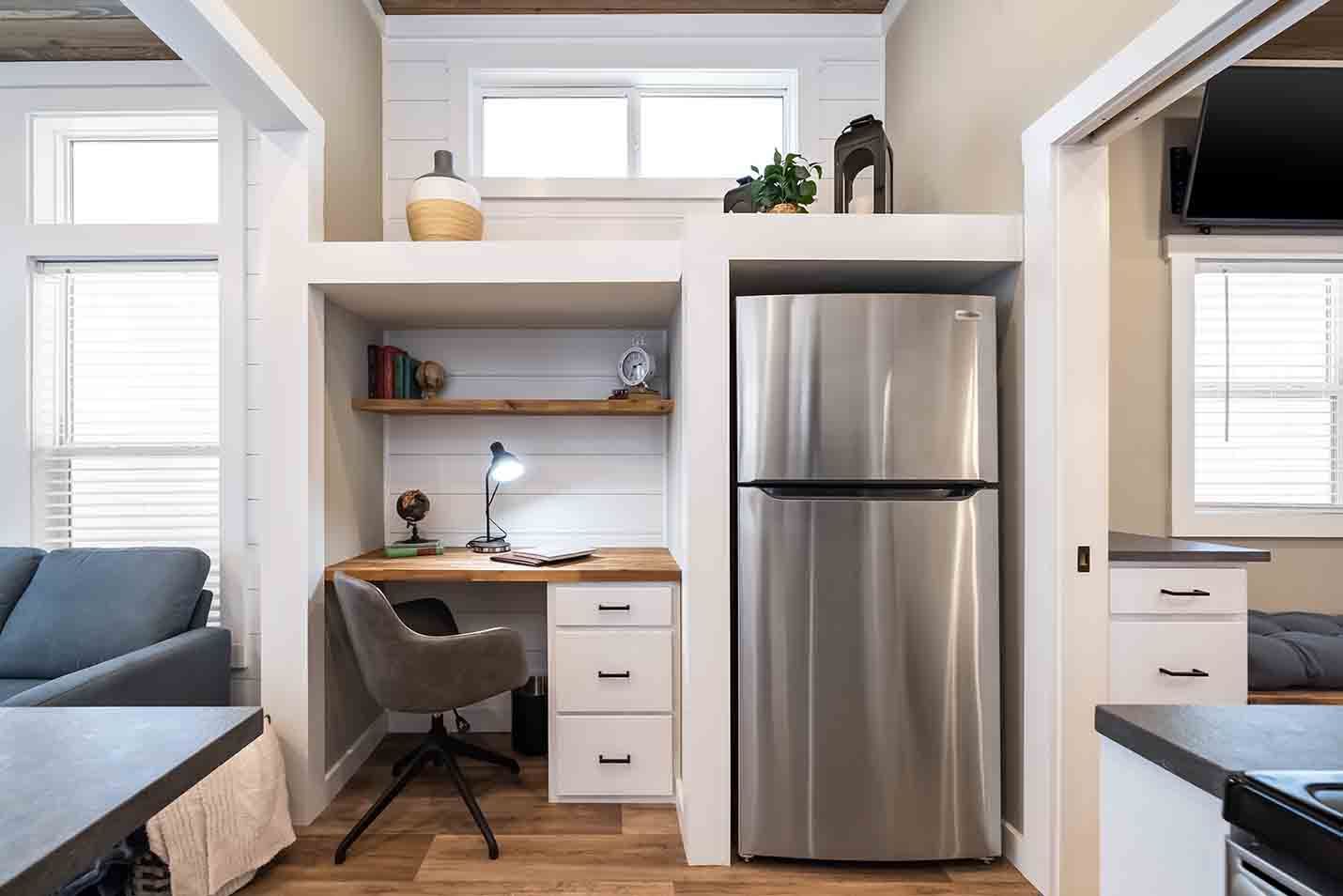 Small modern apartment kitchen nook with stainless steel fridge, desk, and sofa by windows