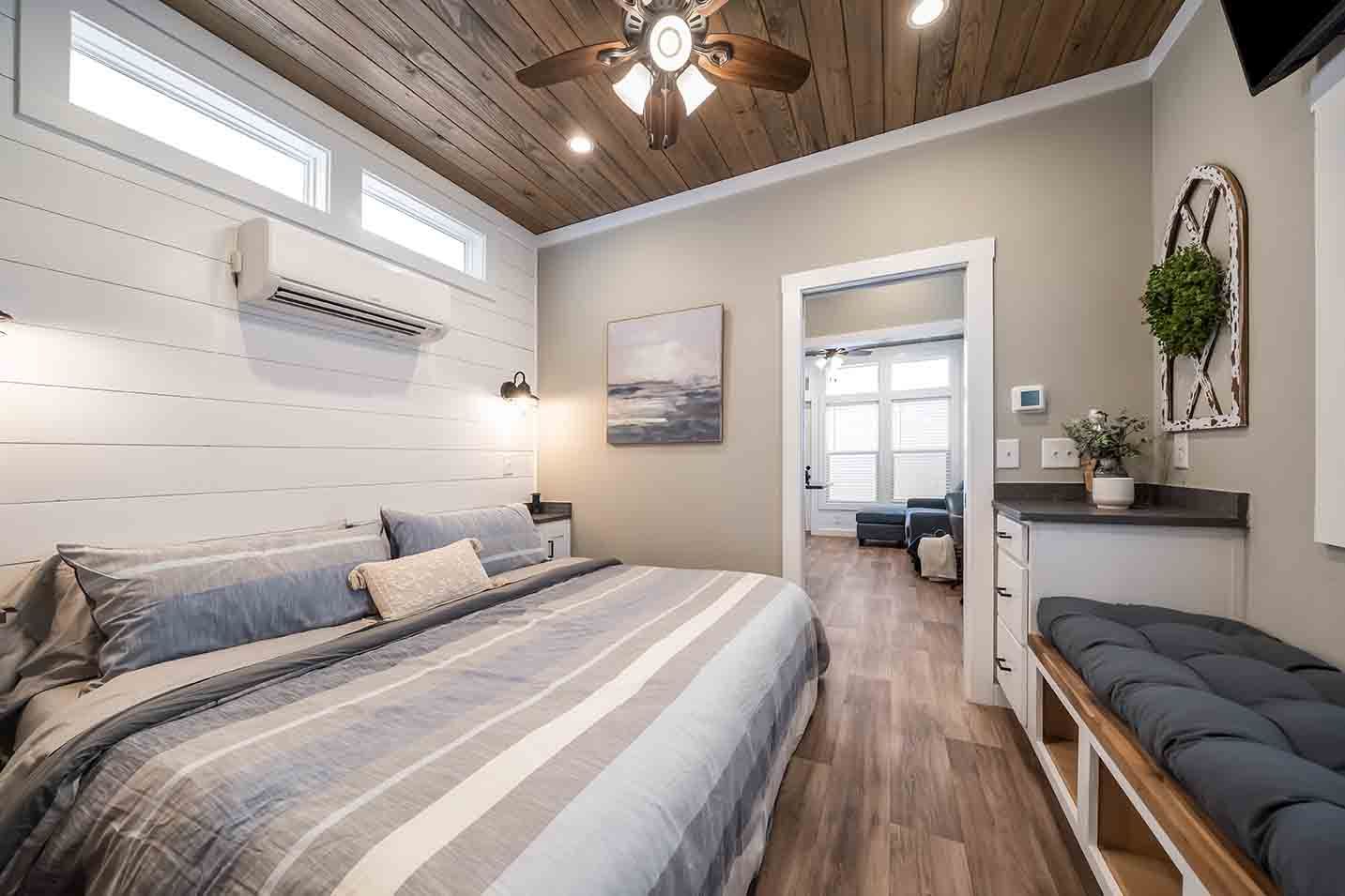 Bright bedroom with a striped bed, wood ceiling, and a bench by the wall
