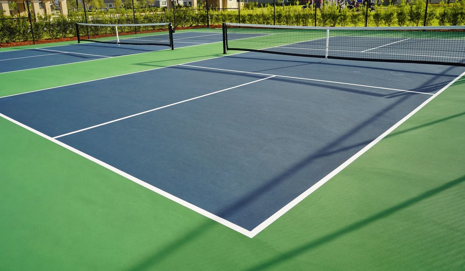 Outdoor pickleball court with blue playing surface, green borders, and a net in the center.
