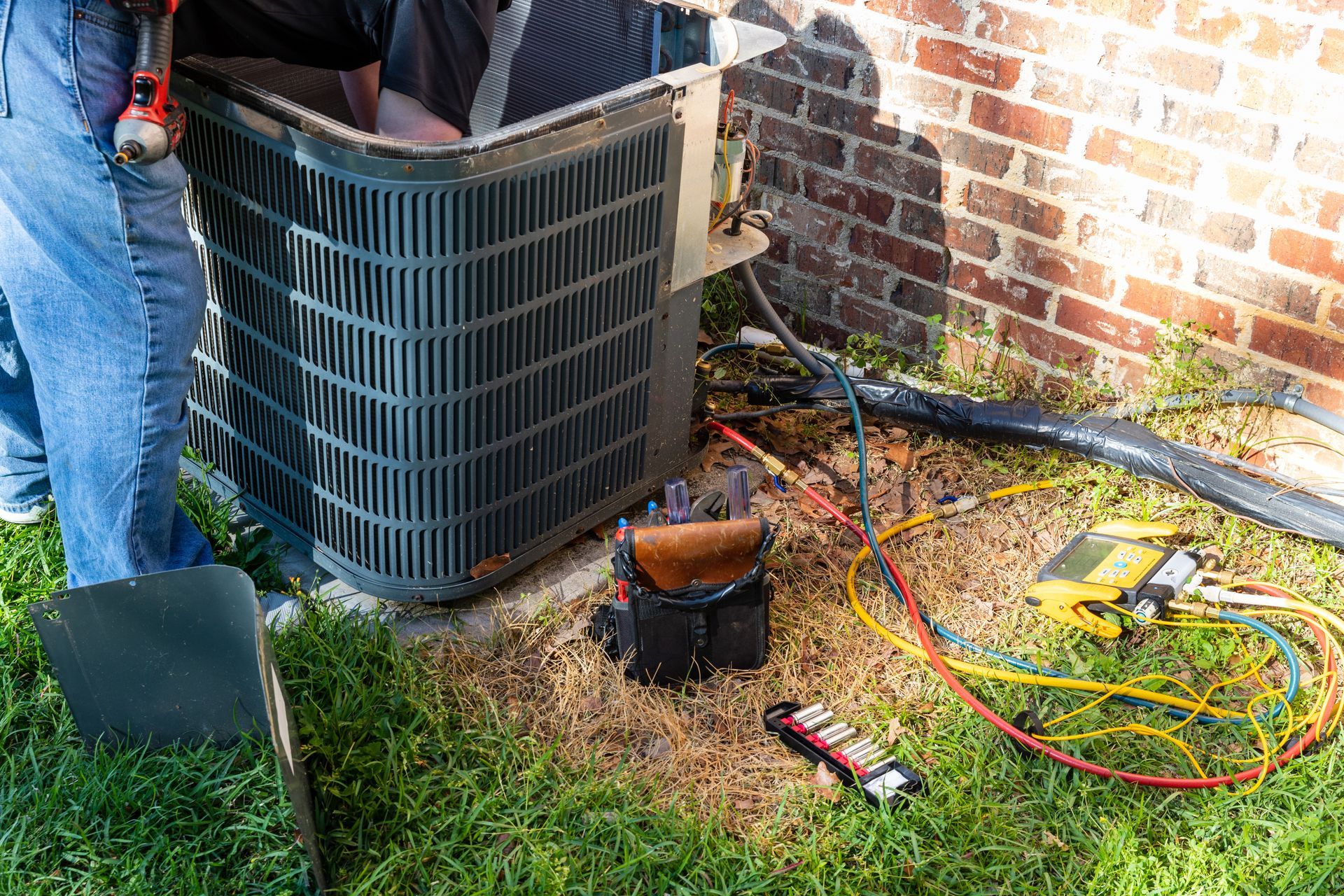 HVAC technician working on an air conditioning unit outside near a brick wall.