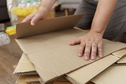 Hands folding a cardboard box among stacked packing materials
