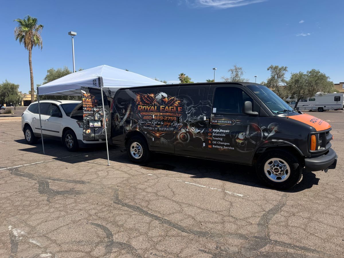 Wrapped service van parked on a suburban street near orange traffic cones and a black truck driveway.