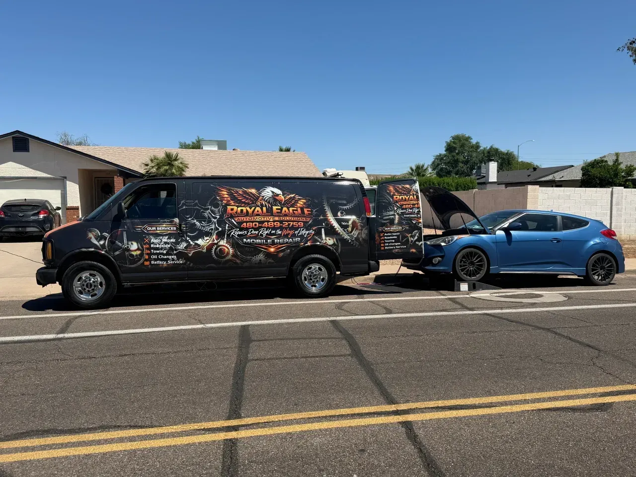 Black van with graphic wrap towing a blue sports car on a sunny suburban street