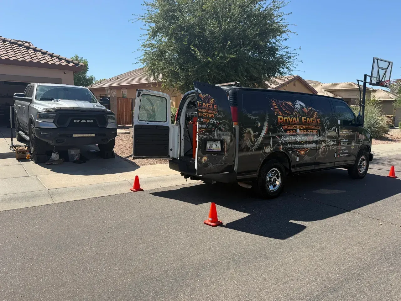 Wrapped service van parked on a suburban street near orange traffic cones and a black truck driveway.