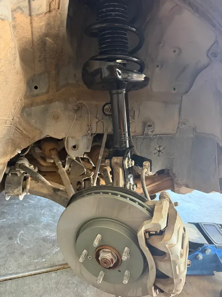 Car wheel well with exposed suspension, strut, brake rotor, and caliper during repair