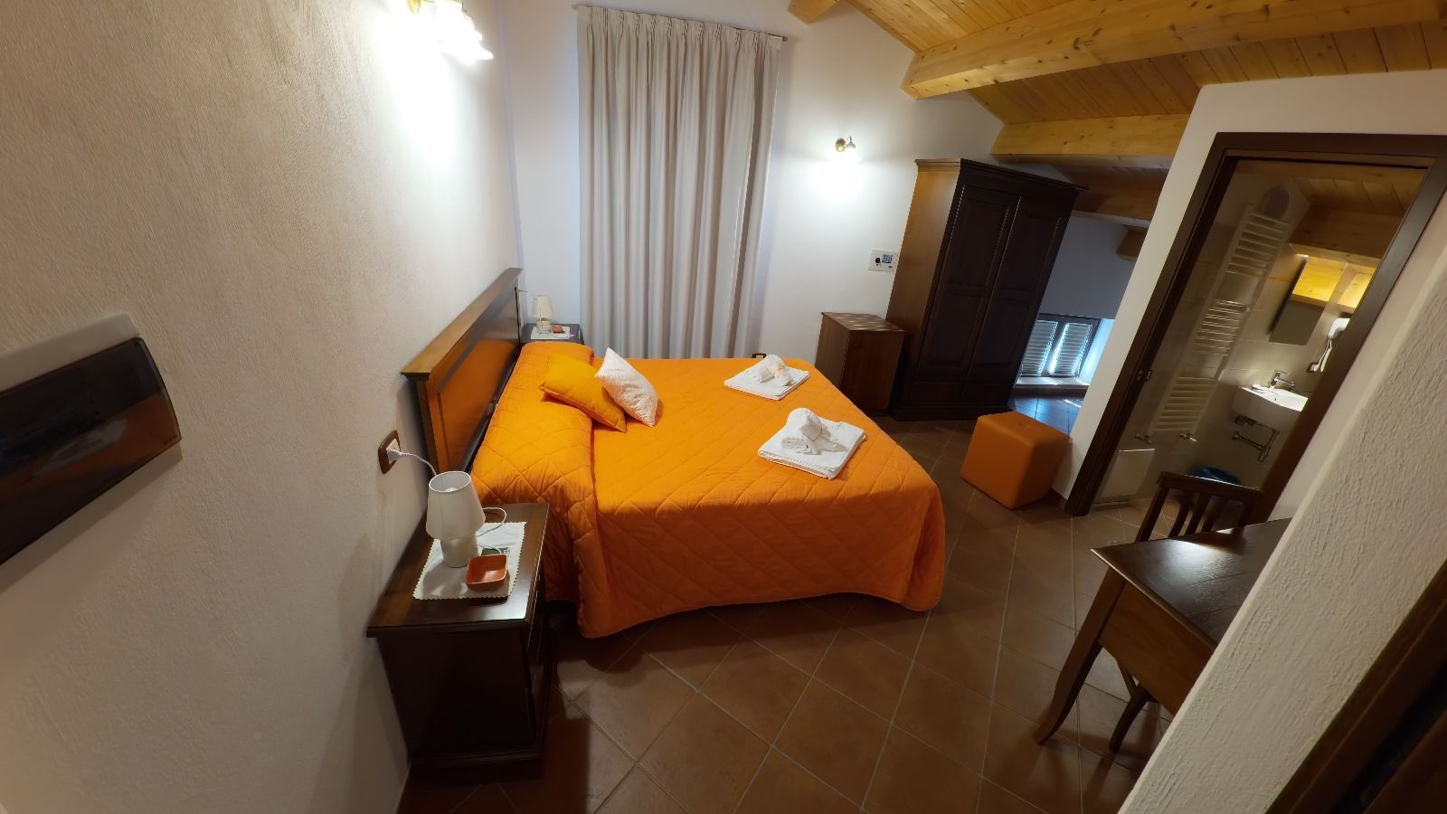 Camera da letto con copriletto arancione, mobili in legno e una porta aperta sul bagno.