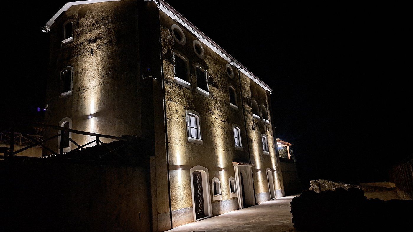 Edificio in pietra a tre piani illuminato di notte con faretti sulla facciata e una strada buia.