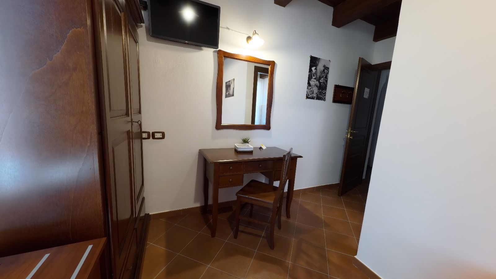 Una camera d'albergo con una cassettiera in legno, uno specchio, una TV e un armadio, su un pavimento piastrellato.