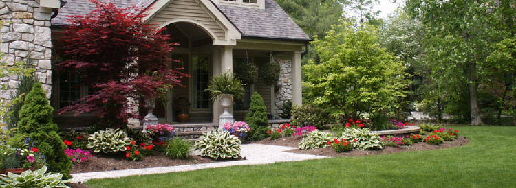 Charming house with arched porch, colorful flower beds, and a manicured green lawn