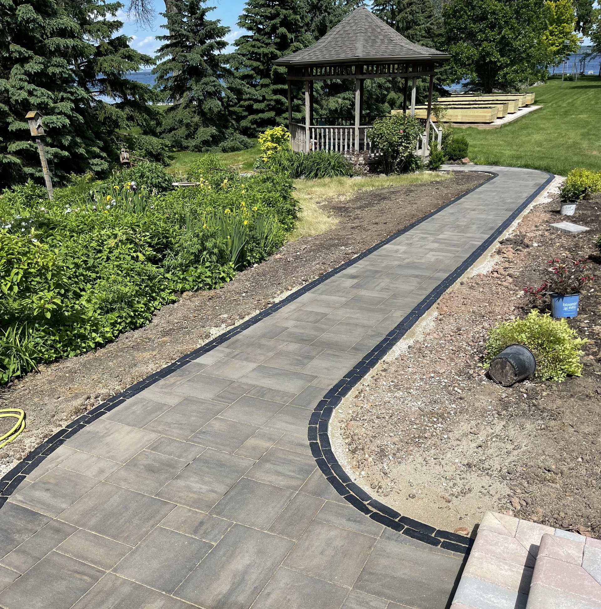 Curved stone garden path leading to a gazebo in a landscaped yard on a sunny day