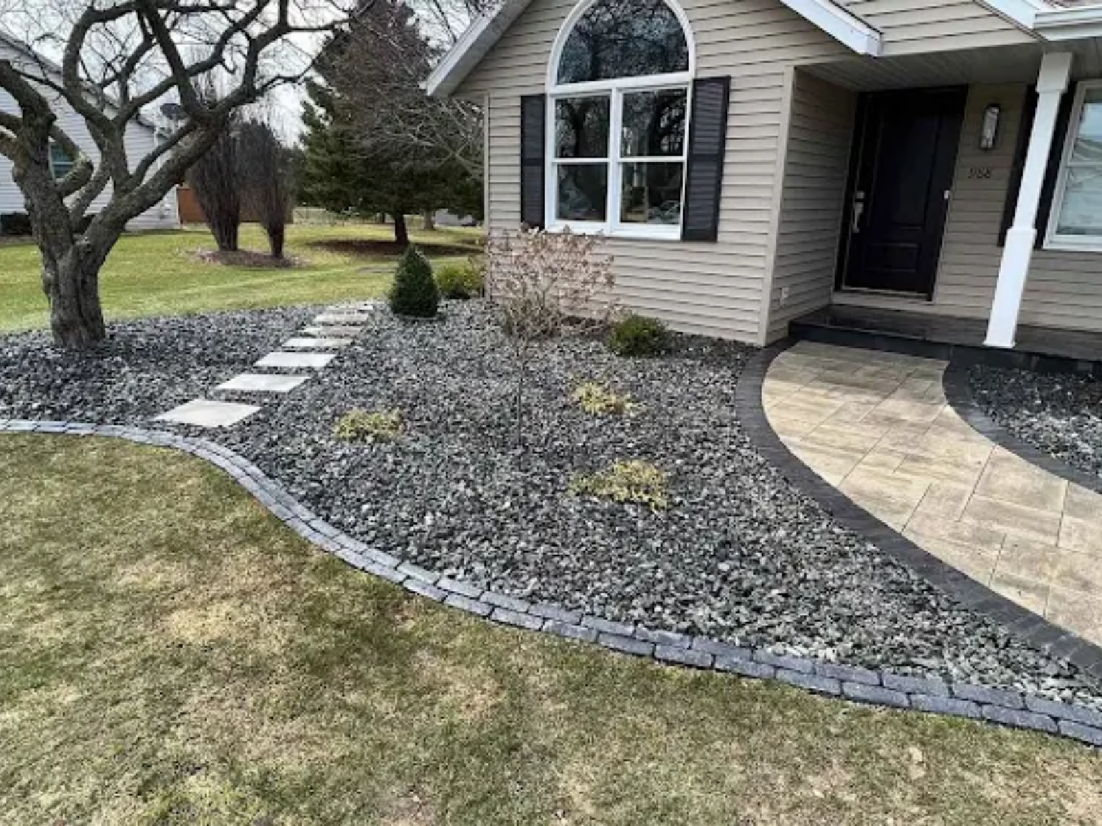 Front yard landscaping with gray rock mulch, stepping stones, and a beige house entryway