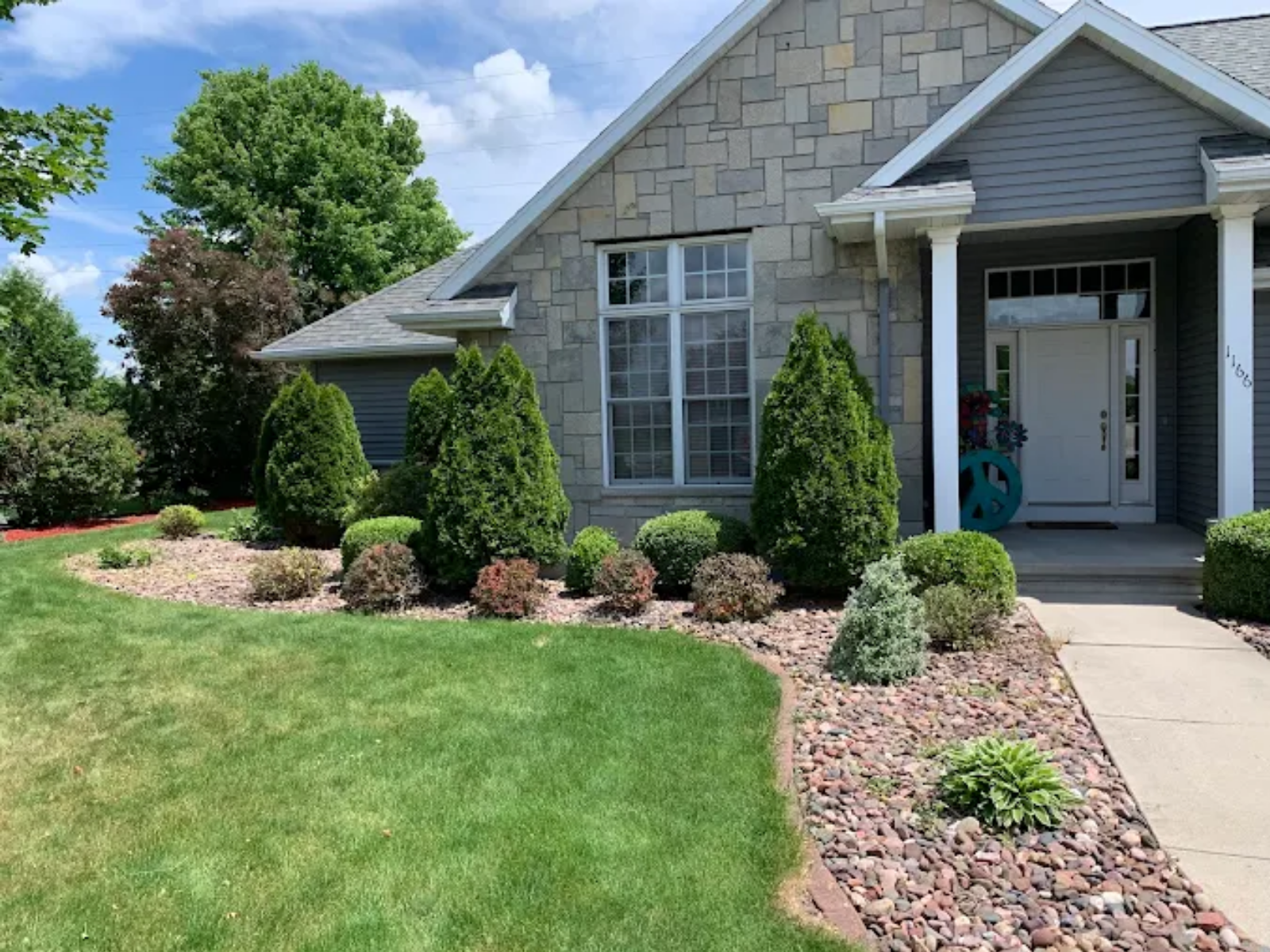 Suburban house with manicured lawn, stone landscaping, and a front porch under a blue sky