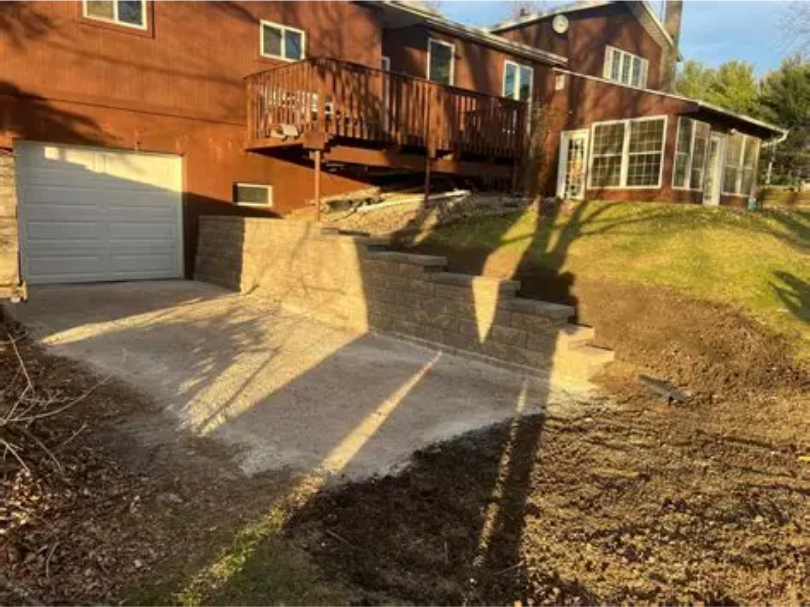 Brick house with garage, driveway, and front deck in warm sunlight