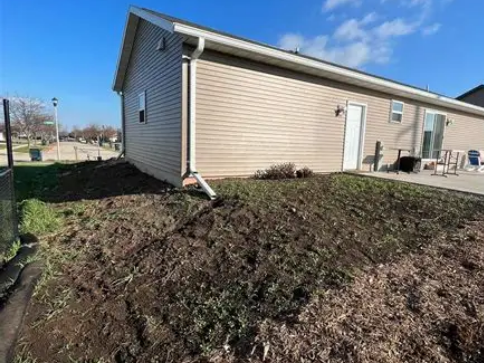 Tan house exterior with muddy, freshly landscaped yard under a blue sky