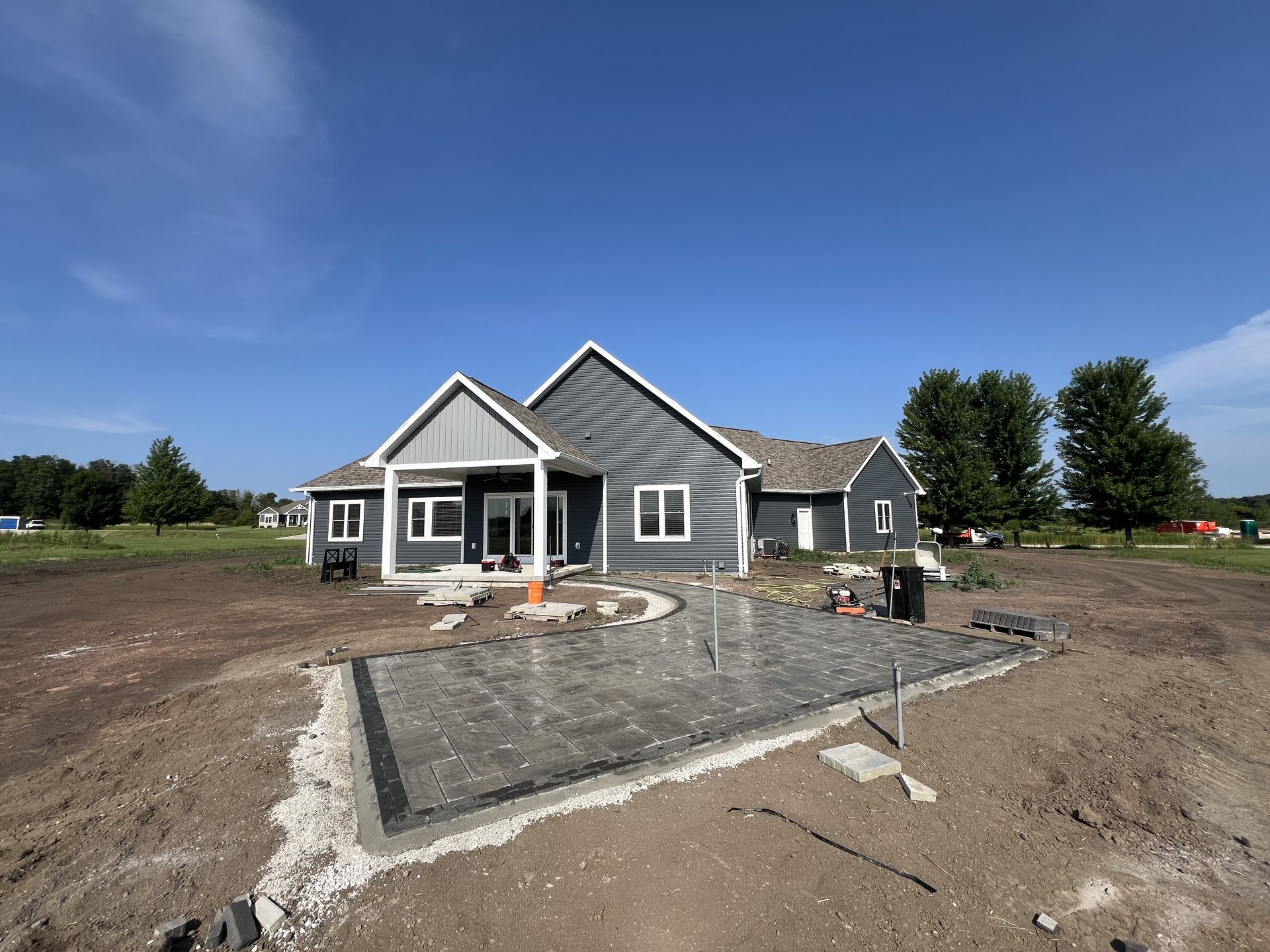 Gray house under construction on a dirt lot, with a fenced patio area and blue sky.
