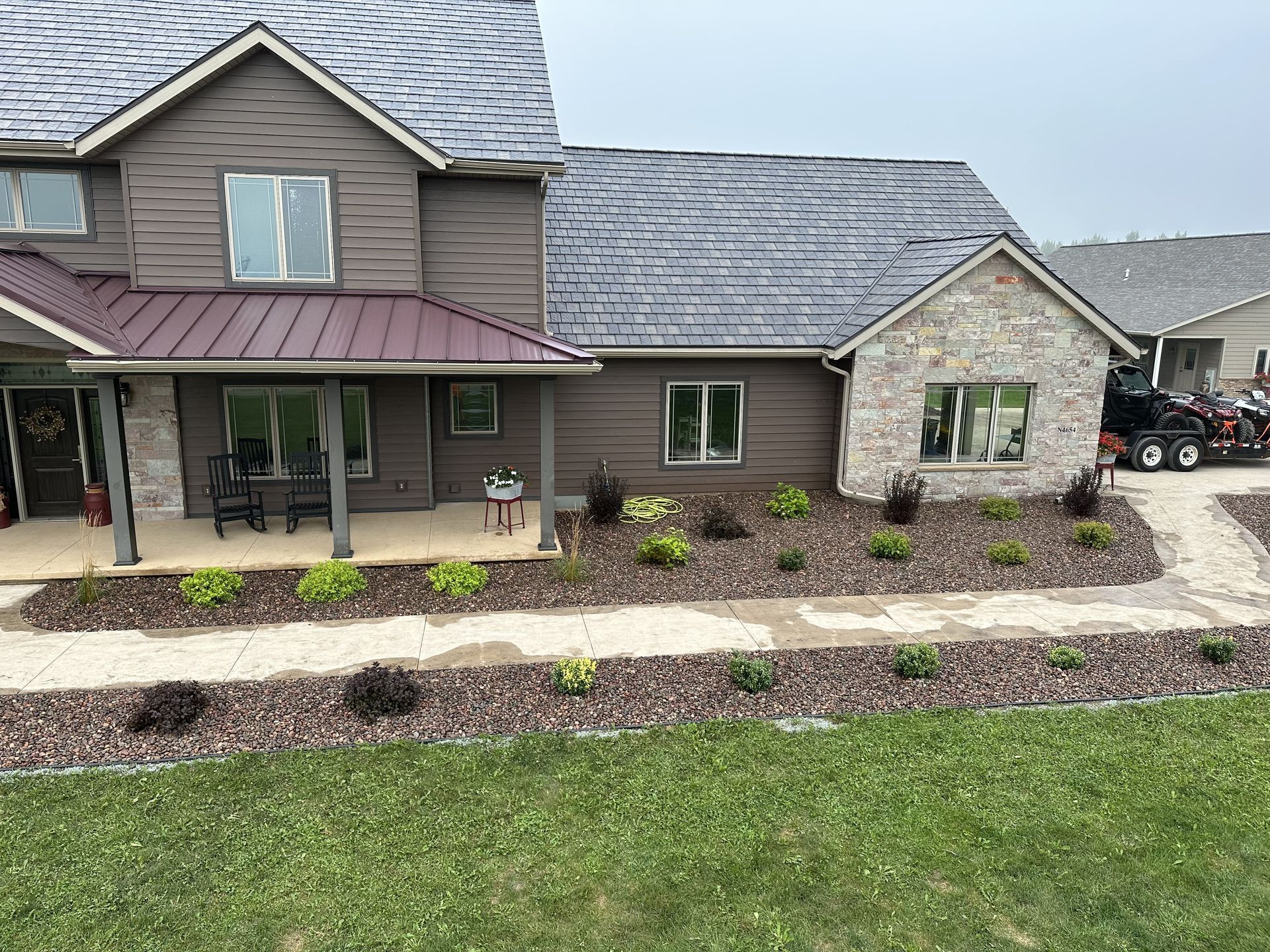 Suburban house with gray siding, front porch, landscaped beds, and a driveway with parked vehicles