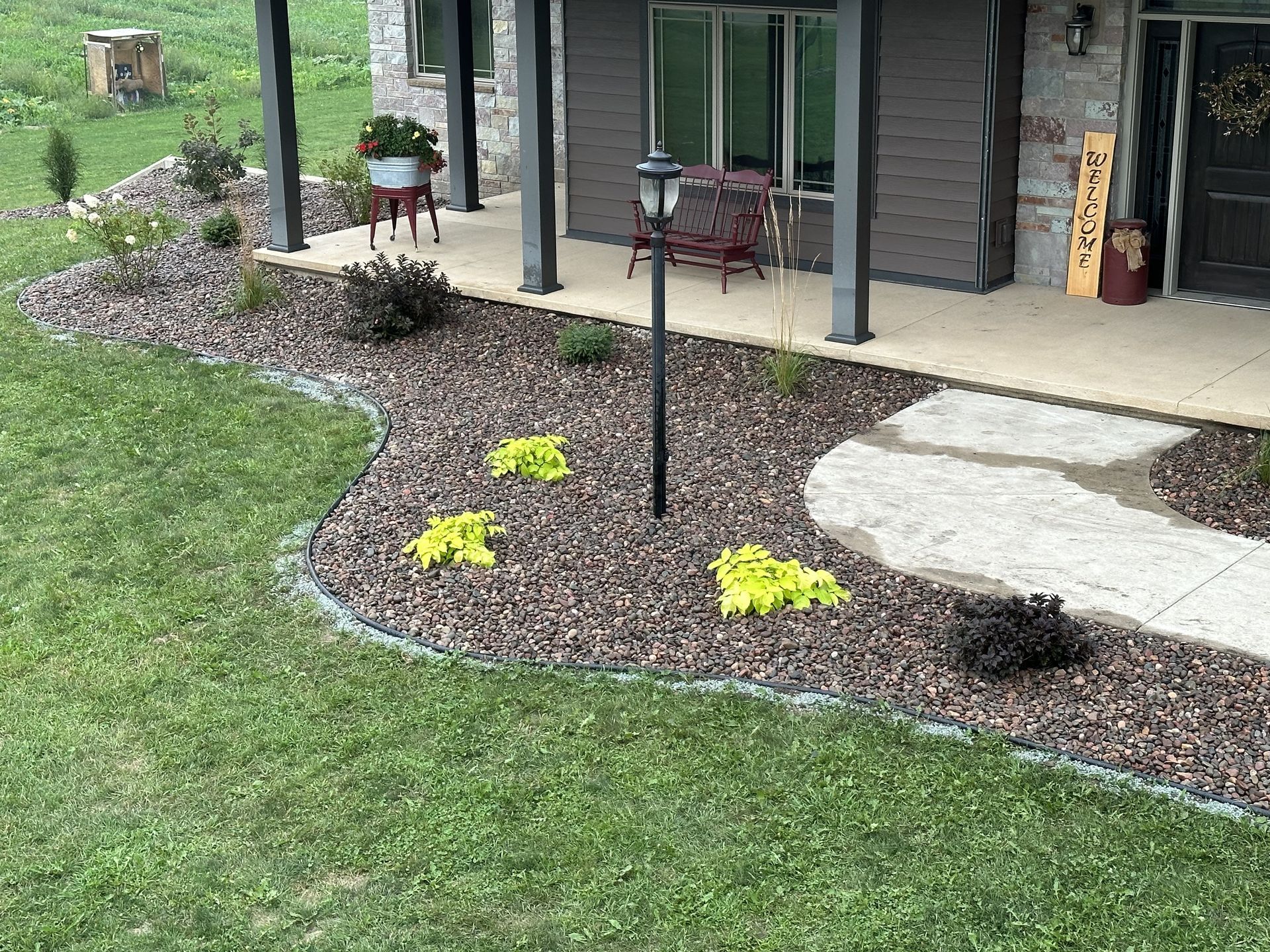 Front yard landscaping with curved mulch beds, yellow flowers, green lawn, and a porch in the background