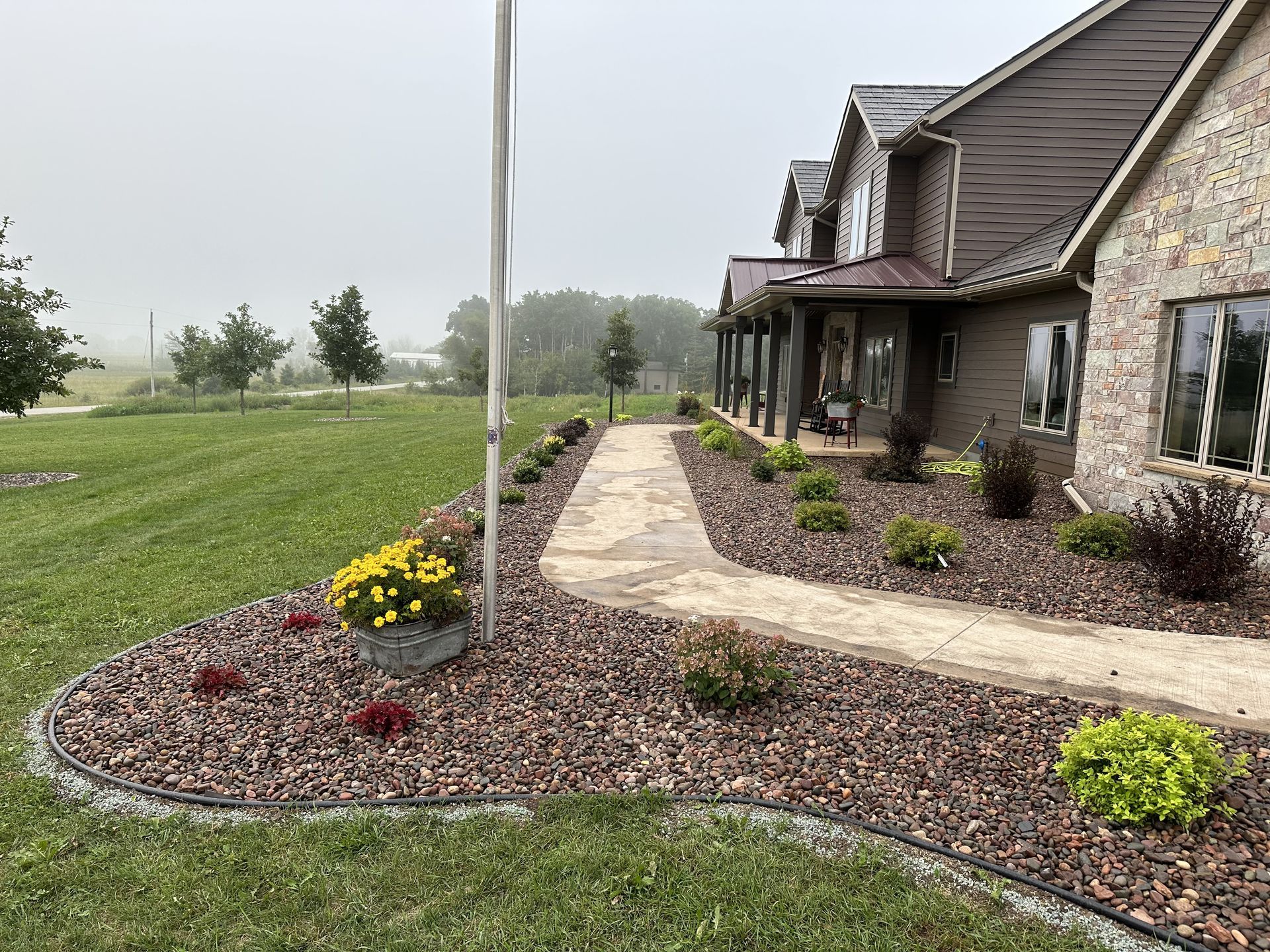 Landscaped stone walkway beside a stone house and lawn under a gray sky