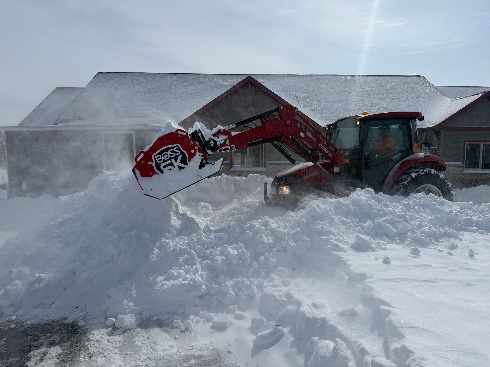 Black car buried in a large snowbank beside a brick building, with a shoveled path in front