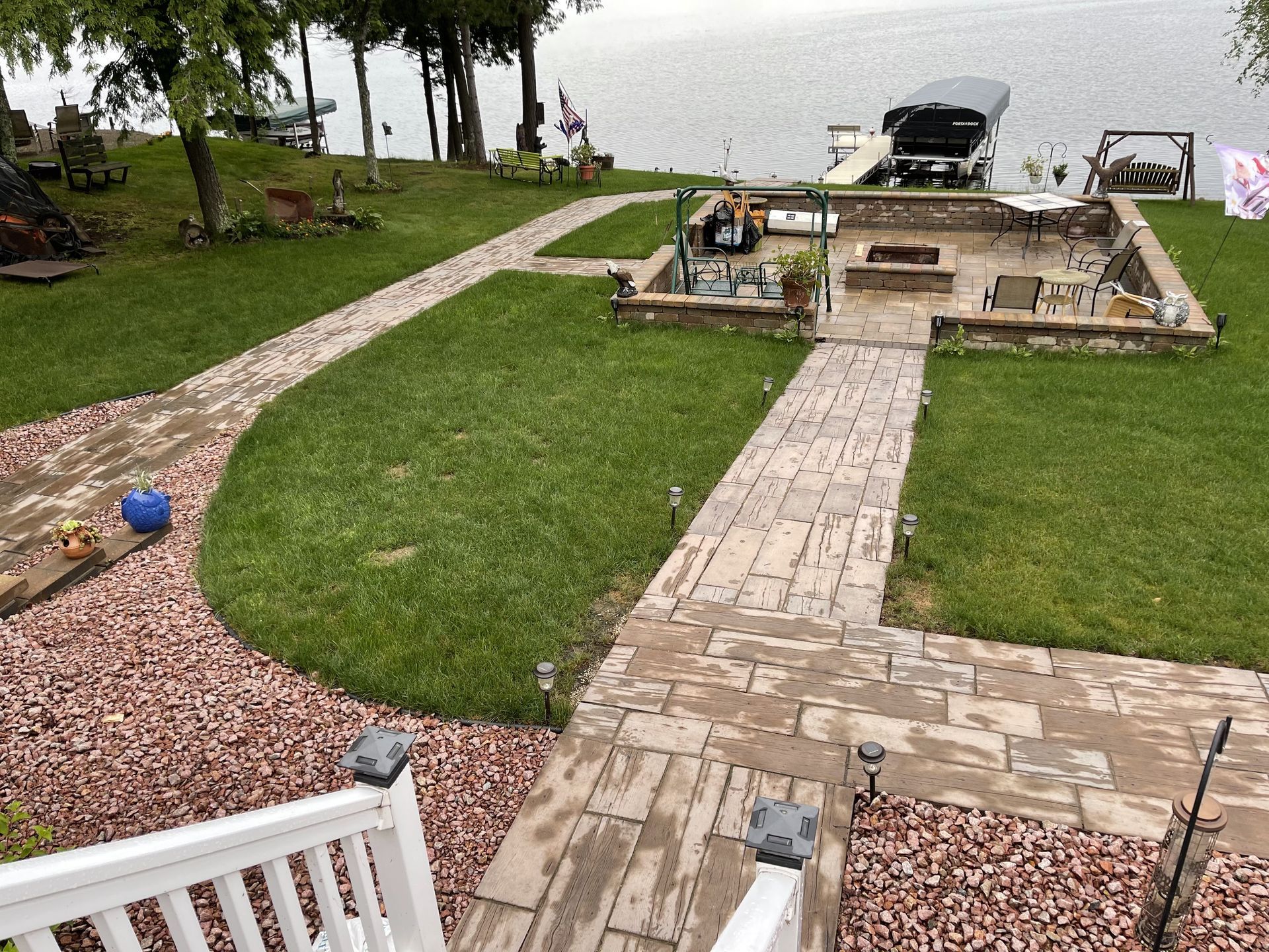 Backyard patio and lawn by a lake, with stone paths, a fire pit, dock, and boat lift