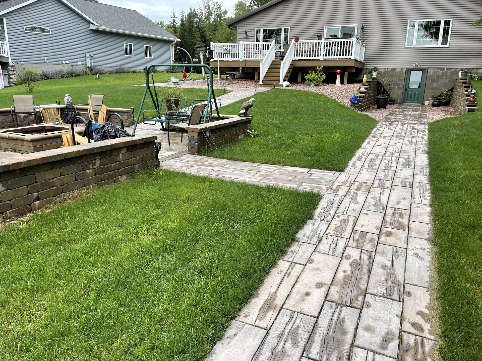 Backyard with stone walkway, raised garden beds, and a house deck in the background