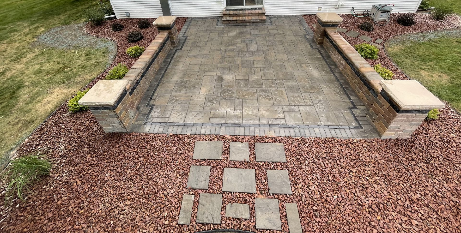 Front yard with green lawn, curved rock mulch bed, shrubs, and a concrete walkway to the house entrance