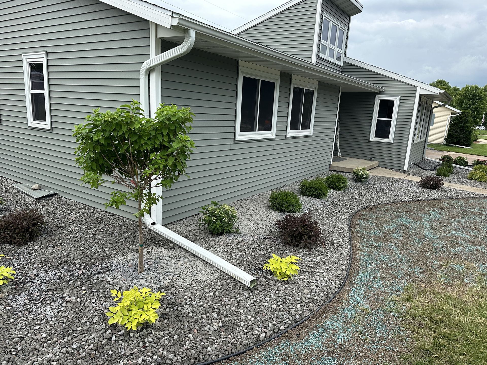 Gray house exterior with white trim and landscaped gravel front yard with small shrubs and yellow flowers