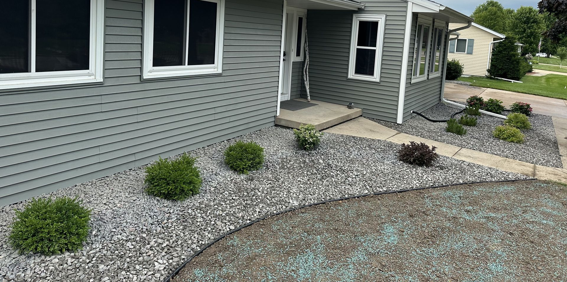 Garden bed with black mulch, large flat stones, colorful flowers, and green grass border