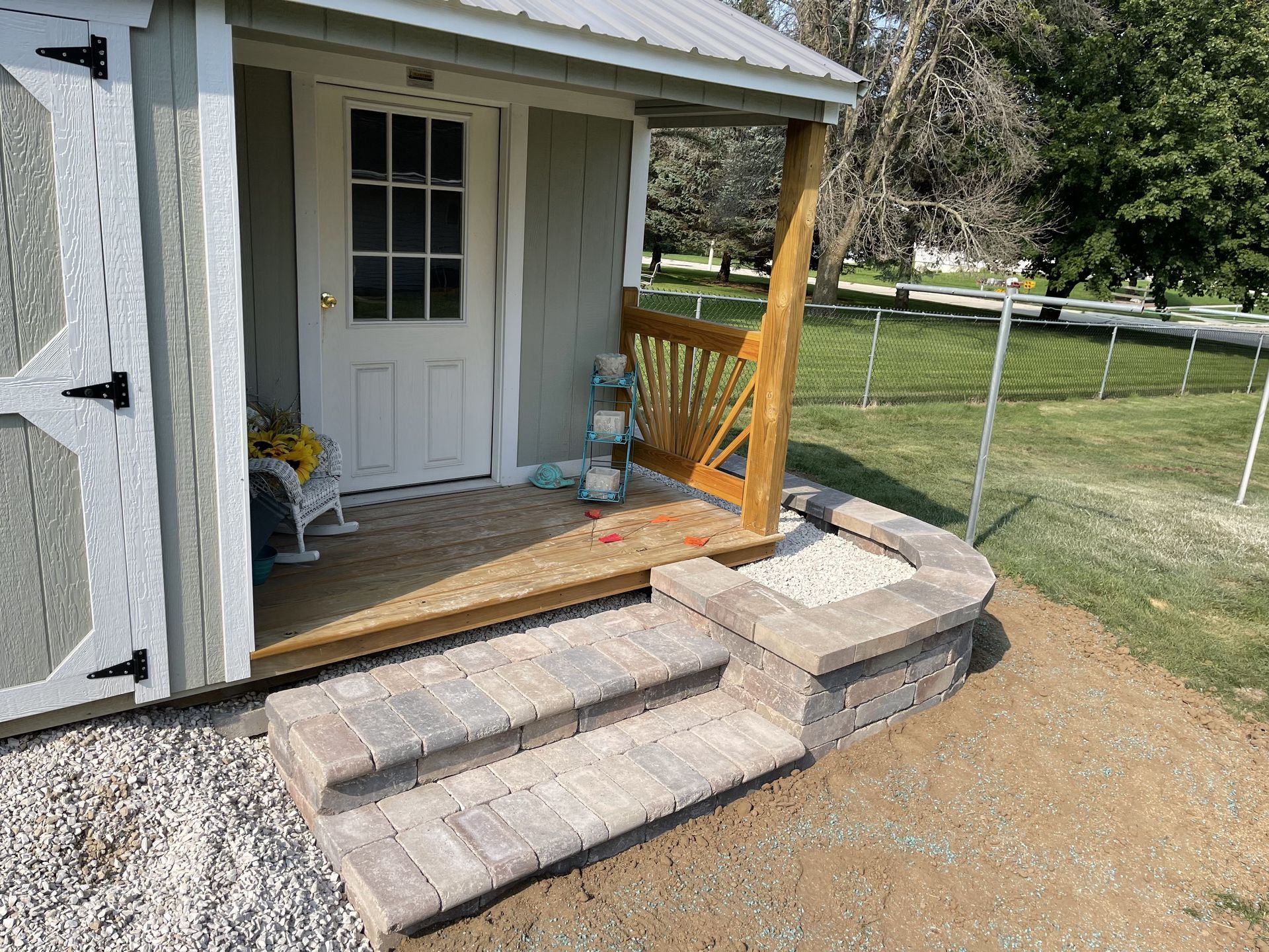 Front porch with a white door, small wooden steps, and a concrete wheelchair ramp beside a chain-link fence.