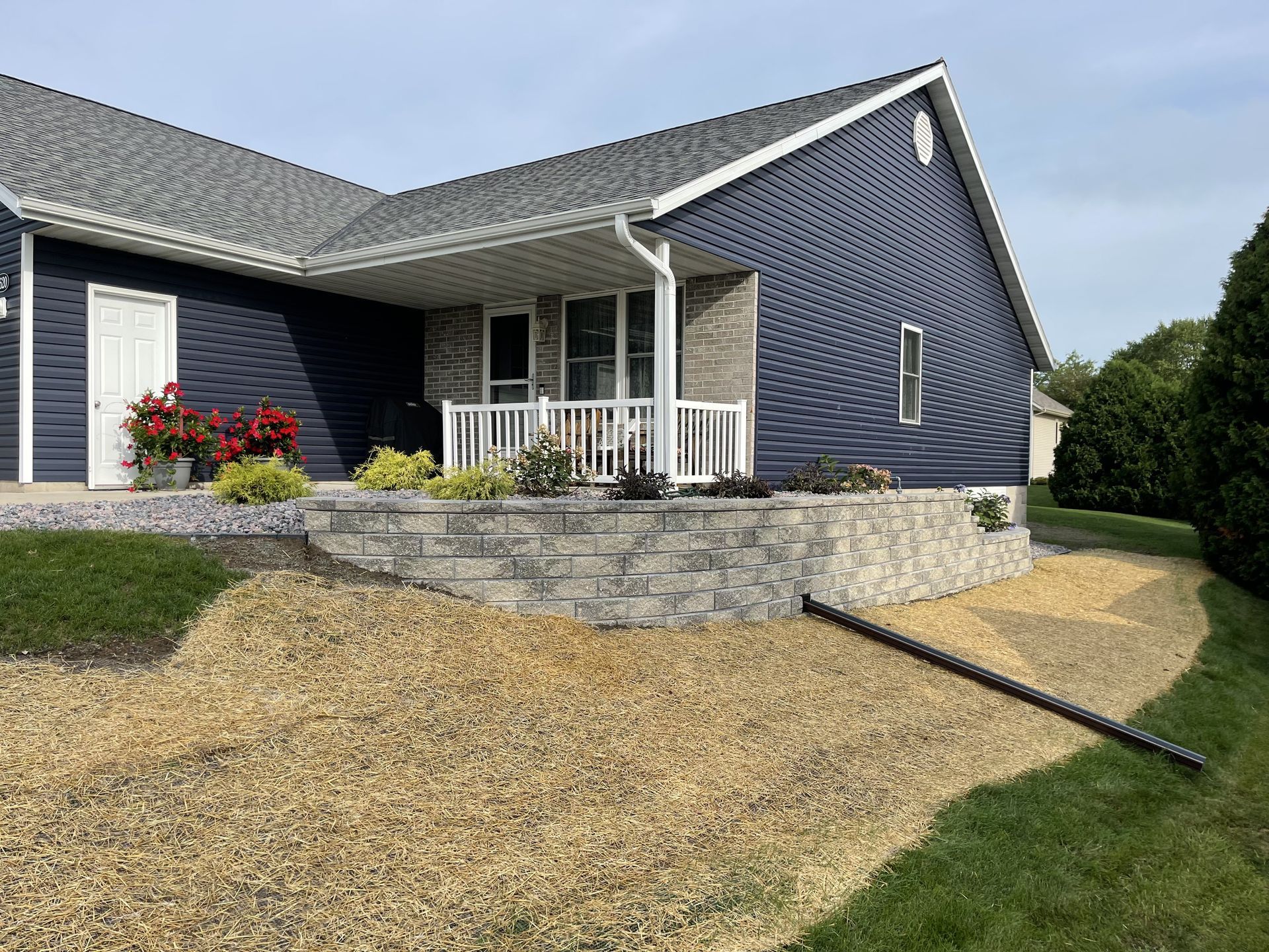 Single-story blue house with stone retaining wall and gravel front yard